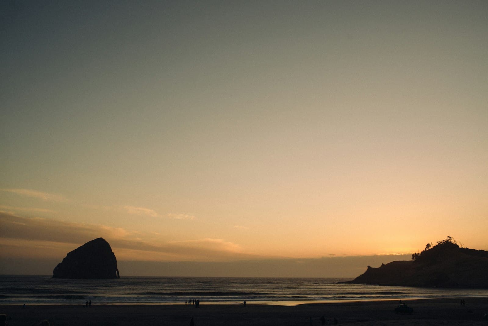 Figures walking the beach at Pacific City at dusk, Haystack Rock on the horizon