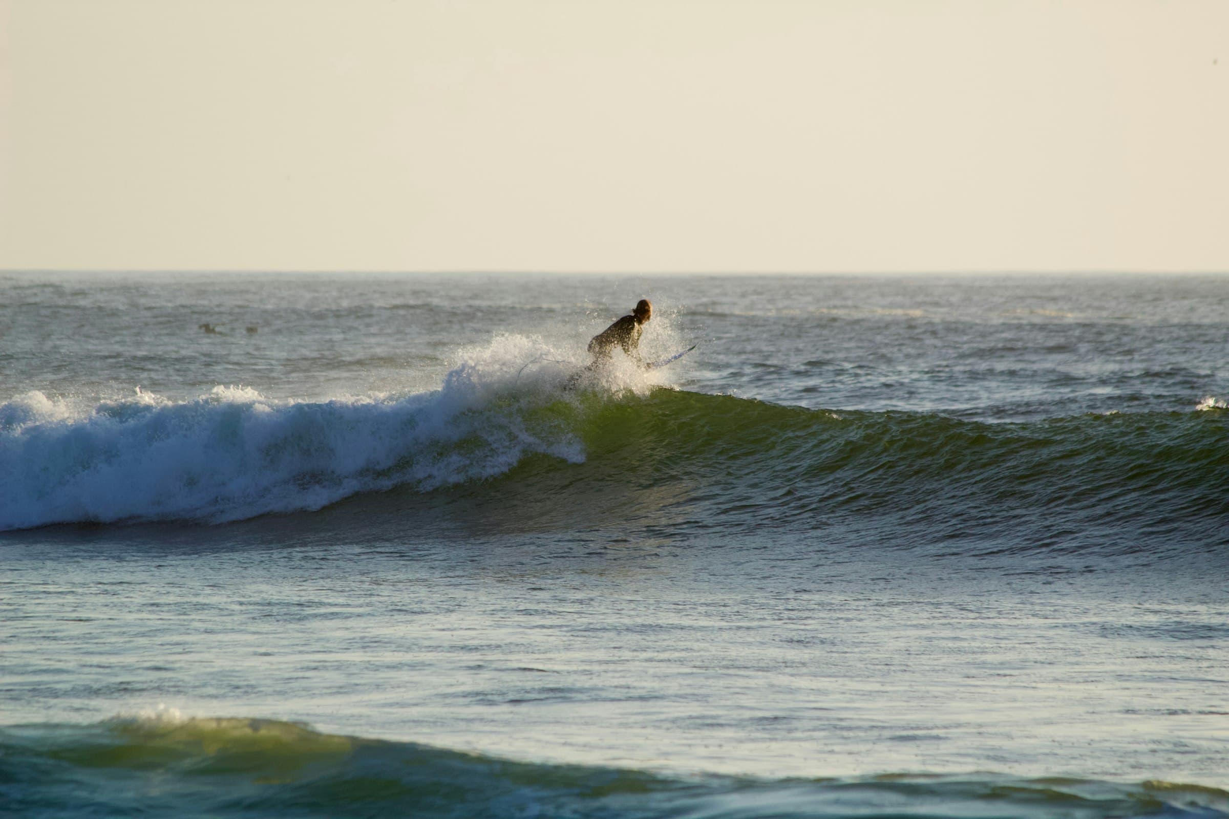 A surfer catching a wave in golden evening light at Pacific City Beach